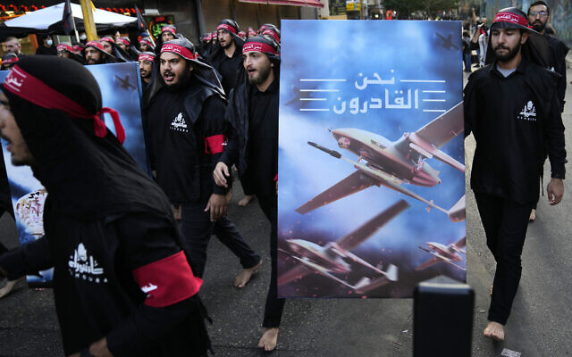 Members of Iranian-backed Hezbollah walk barefoot as they carry a poster showing Hezbollah drones that read, in Arabic 'We are coming,' during the holy day of Ashoura in the southern suburb of Beirut, Lebanon, August 9, 2022. (AP Photo/Hussein Malla, File)