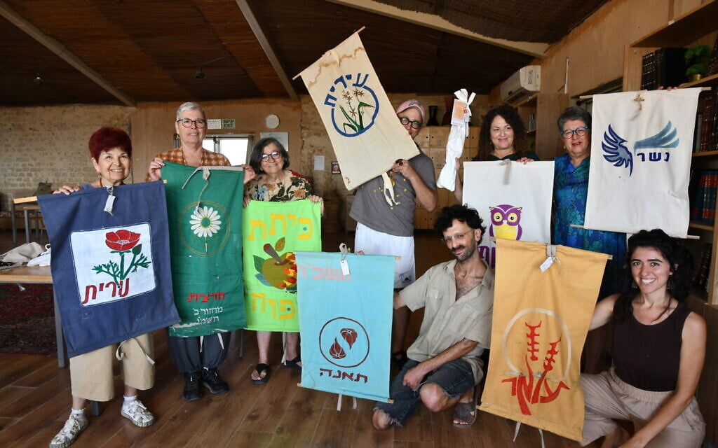 Volunteers involved with the flag repair project pose at Kulna, Yeruham, southern Israel, July 29, 2024. Racheli Schreiber heads Kulna's traditional arts and crafts program and is seated bottom right. Nirit Shalev-Khalifa is standing in the back row, second from right, holding a flag and one of the new storage bags. (Sarit Uziely)