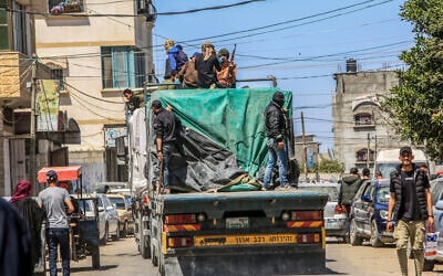Armed and masked Palestinians sit on trucks leading humanitarian aid into Gaza through the Kerem Shalom Crossing with Israel, in the Strip's south, April 3, 2024. (Abed Rahim Khatib/Flash90)