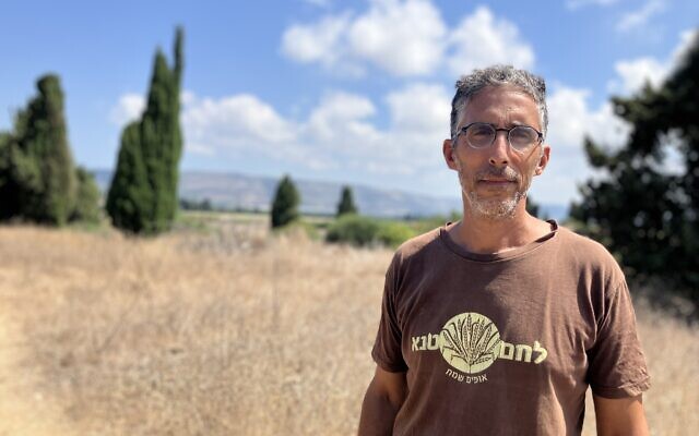 David Amzel, owner of Lechem Tene Bakery in Gesher Haziv, stands in the kibbutz with the border of Lebanon behind him on August 15, 2024. (Diana Bletter/The Times of Israel)