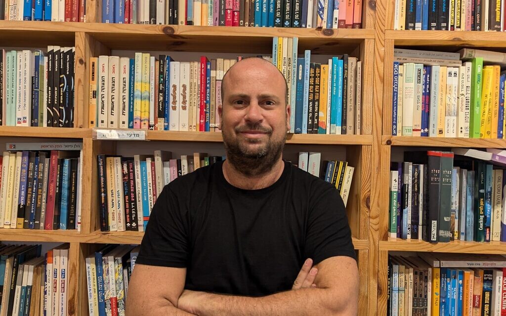 Eyal Levkovich stands against the books of his store, Goldmund Books, in Haifa on August 4, 2024. (Canaan Lidor/Times of Israel)