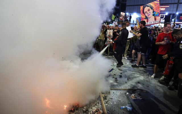 A police officer puts out a fire set by demonstrators during an anti-government protest calling for action to secure the release of hostages held captive by Hamas since October 7, Tel Aviv on September 7, 2024. (Jack Guez/AFP)