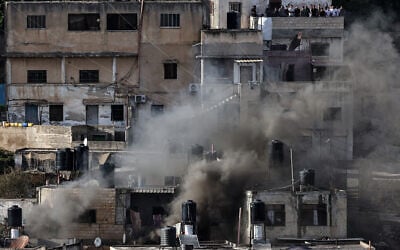 People watch from a balcony as smoke billows during an IDF raid in the northern West Bank city of Qabatiya, September 19, 2024. (Zain Jaafar/AFP)