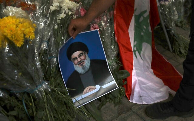 A man places a poster of Hezbollah leader Sayyed Hassan Nasrallah near bouquets of flowers in front of the Lebanese Embassy in Tehran, Iran, September 18, 2024. (AP Photo/ Vahid Salemi)