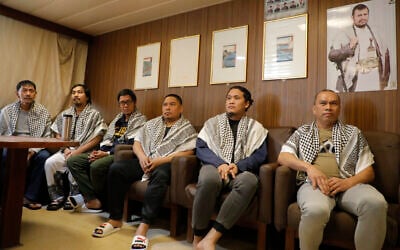 The crew of the Israeli Galaxy ship, which was seized by the Houthi group, sit under a poster of the Houthi leader Abdul-Malik Badruldeen al-Houthi, on their ship in the port of Saleef, near Hodeidah, Yemen, May 12, 2024. (AP Photo/Osamah Abdulrahman)