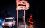 An Israeli soldier stands near the scene of a car bomb explosion in the West Bank settlement of Karmei Tzur, in front of a sign in which the Arabic has been blacked out by vandals, August 31, 2024. (Yonatan Sindel/Flash90)