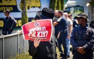 An ultra-Orthodox Jew protesting against the drafting of Haredim to the Israeli army holds a sign reading, 'We won't draft to an enemy army,' outside the IDF Recruitment Center at Tel Hashomer, in central Israel, September 2, 2024. (Avshalom Sassoni/Flash90)