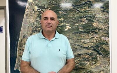 Moshe Davidovich, head of the Mateh Asher Regional Council, stands in front of a map of the region in his office on September 23, 2024. (Diana Bletter/The Times of Israel)