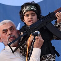 Hamas leader Yahya Sinwar holds the child of an Al-Qassam Brigades fighter with a Kalashnikov rifle in his hand during a rally in Gaza City on May 24, 2021. (Emmanuel Dunand/AFP)