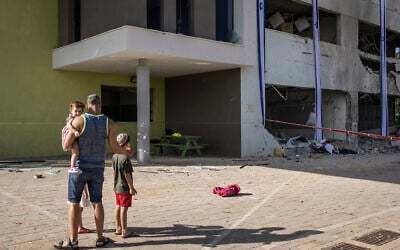 A father shows his children a school in Israel's southern city of Gedera on October 2, 2024, after it was hit during the previous day's barrage of ballistic missiles fired at Israel by Iran. (JOHN WESSELS / AFP)