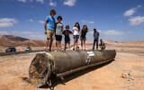 Israelis stand on top of the remains of an Iranian missile in the Negev desert near Arad, on October 2, 2024, in the aftermath of an Iranian missile attack on Israel. (Menahem Kahana/AFP)