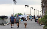 Lebanese men walk with a dog past tents where displaced people have been sleeping on Beirut's seaside promenade of Ain al-Mreisseh, on October 7, 2024. (Anwar AMRO / AFP)