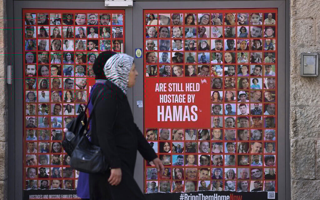 Women walk past a store entrance displaying a banner with the portraits of hostages held in Gaza since October 7, 2023, in Jerusalem's King George street on October 13, 2024. (Hazem Bader/AFP)
