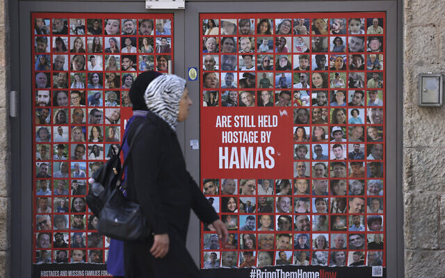 Women walk past a store entrance displaying a banner with the portraits of hostages held in Gaza since October 7, 2023, in Jerusalem's King George street on October 13, 2024. (Hazem Bader/AFP)