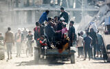 People ride in the back of and atop a truck moving past destroyed buildings in the Al-Mawasi area of Khan Younis in the southern Gaza Strip on October 23, 2024. (Bashar Taleb / AFP)