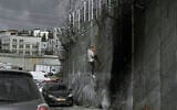 A Palestinian man climbs the security barrier at the West Bank town of al-Ram to cross into Israel illegally, on September 15, 2024. (AP Photo/ Mahmoud Illean/ File)