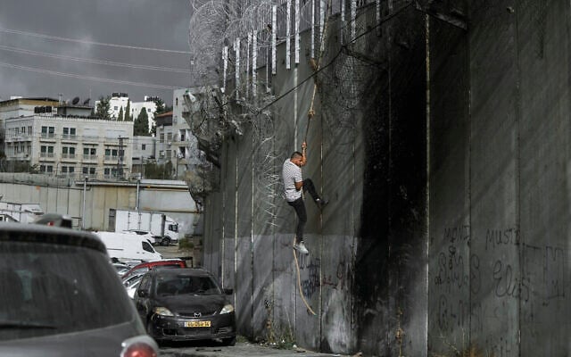 A Palestinian man climbs the security barrier at the West Bank town of al-Ram to illegally cross into Israel, September 15, 2024. (AP Photo/Mahmoud Illean) A Palestinian man climbs the security barrier at the West Bank town of al-Ram to illegally cross into Israel, September 15, 2024. (AP Photo/Mahmoud Illean)