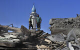 A Hezbollah rescue worker, left, and a Lebanese civil defense worker, right, stand on the rubble of destroyed buildings at a commercial street that was hit Saturday night by Israeli airstrikes, in Nabatiyeh town, south Lebanon, Sunday, Oct. 13, 2024. (AP Photo/Mohammed Zaatari)