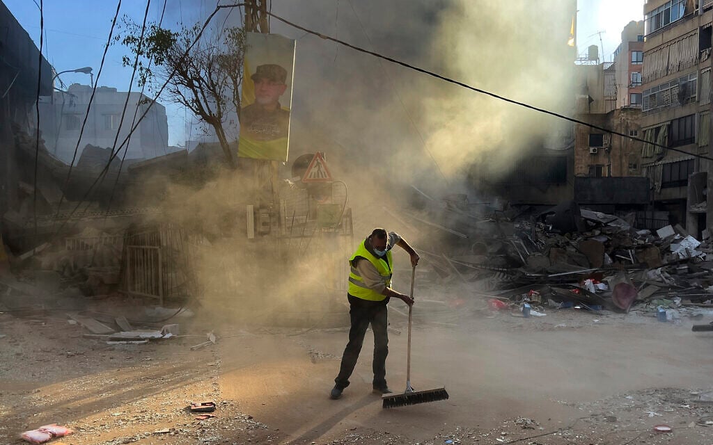 A worker cleans a street as smoke rises from a destroyed building that was hit by an Israeli airstrike in Dahiyeh, in the southern suburb of Beirut, Lebanon, October 20, 2024. (AP Photo/Hussein Malla)