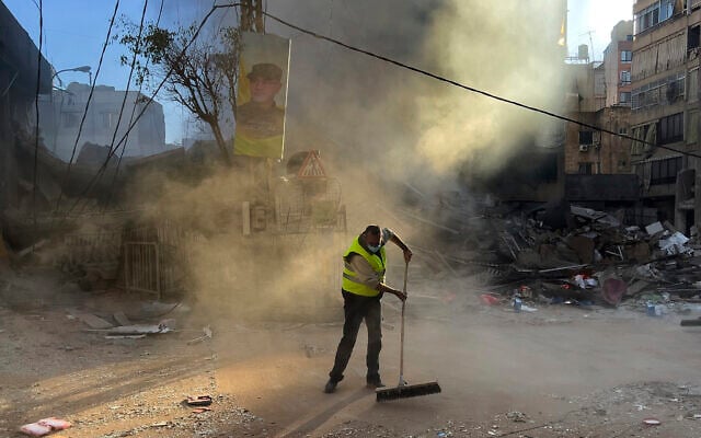 A worker cleans a street as smoke rises from a destroyed building that was hit by an Israeli airstrike in Dahiyeh, in the southern suburb of Beirut, Lebanon, October 20, 2024. (AP Photo/Hussein Malla)