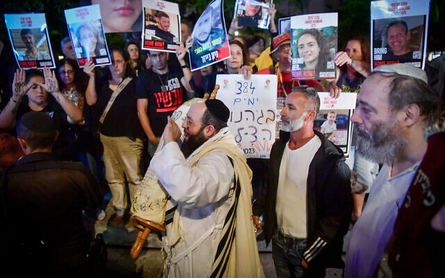 Jewish men carrying Torah scrolls dance by Israeli protesters calling for the release of Israelis held hostage by Hamas terrorists in Gaza, at Dizengoff Square in Tel Aviv, during the Simhat Torah holiday, on October 24, 2024. (Avshalom Sassoni/Flash90)