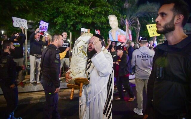 Men carrying Torah scrolls dance by protesters calling for the release of hostages held by Hamas terrorists in Gaza, at Dizengoff Square in Tel Aviv, during the Simhat Torah holiday, October 24, 2024. (Avshalom Sassoni/Flash90) Men carrying Torah scrolls dance by protesters calling for the release of hostages held by Hamas terrorists in Gaza, at Dizengoff Square in Tel Aviv, during the Simhat Torah holiday, October 24, 2024. (Avshalom Sassoni/Flash90)