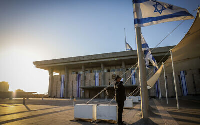 A Knesset guard lowers the Israeli flag to half-staff to commemorate the National Remembrance Day for October 7 massacre and the ongoing war it started in the Gaza Strip, at the Knesset, in Jerusalem, October 27, 2024. (Chaim Goldberg/Flash90)