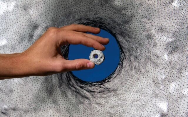 A spindle whorl found at Nahal Ein Gev II, held up in front of a 3D model. (courtesy Hebrew University/Daniel Rolider for Smithsonian-Magazine)