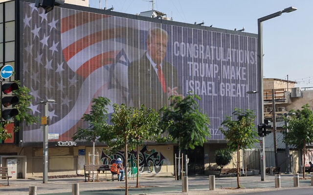 A man sits on a public bench beneath a large billboard congratulating Donald Trump in Tel Aviv on November 6, 2024.(Photo by Jack GUEZ / AFP) A man sits on a public bench beneath a large billboard congratulating Donald Trump in Tel Aviv on November 6, 2024.(Photo by Jack GUEZ / AFP)
