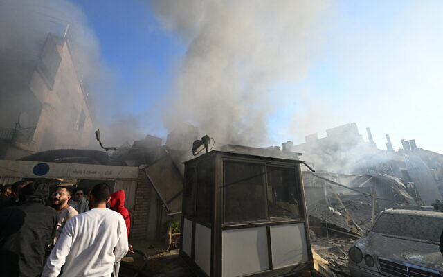 People check the damage as smoke billows from a building hit by a reported Israeli strike in the Mazzeh district of Damascus on November 14, 2024.  (Photo by LOUAI BESHARA / AFP)