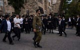 Illustrative: An IDF soldier walks among Haredi men during a protest in Jerusalem against a potential new draft law that they fear could end their exemptions from military service, October 31, 2024. (AP/Ohad Zwigenberg)