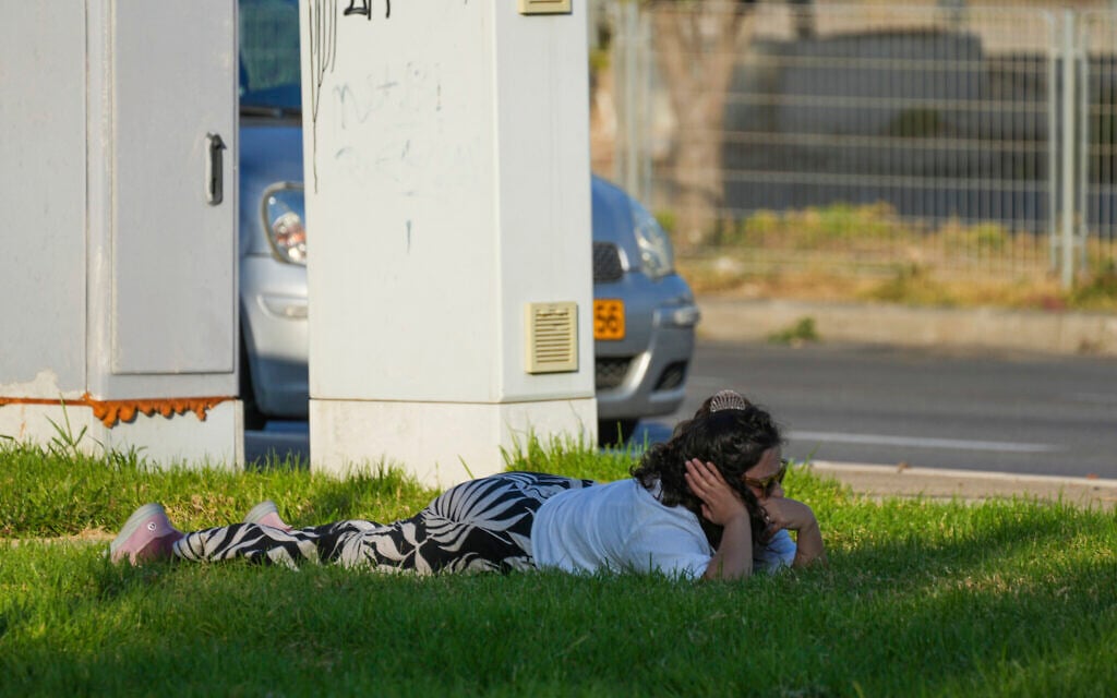 A woman takes cover as a siren sounds a warning of incoming rockets fired from Lebanon, in Kiryat Yam, northern Israel, Wednesday, Nov. 13, 2024. (AP Photo/Ohad Zwigenberg)