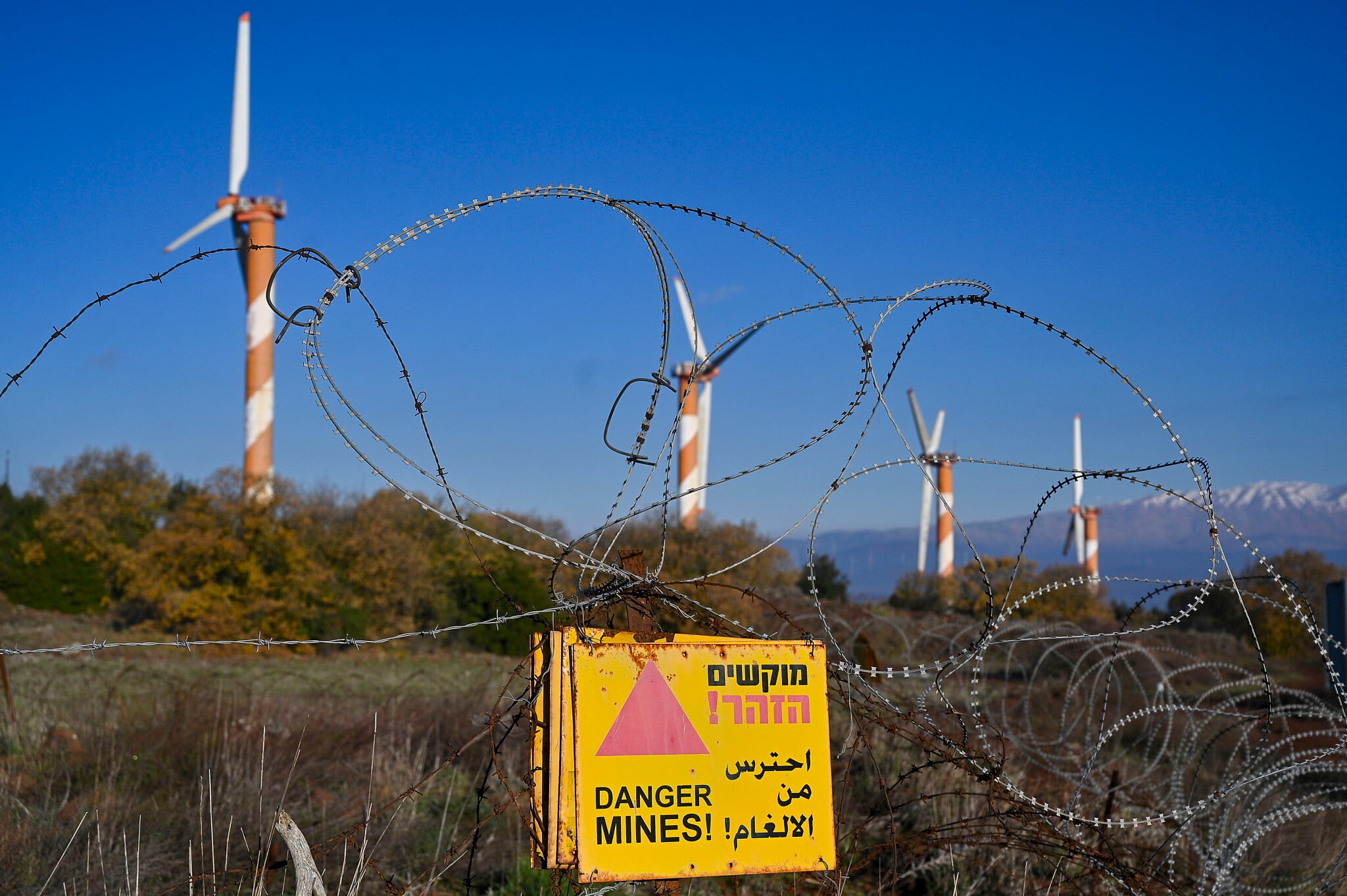 Renewable energy wind turbines as seen next to the snowy peaks of Mount Hermon on January 3, 2021, northern Golan Heights, with a posted sign warning of land mines. (Michael Giladi/Flash90) Renewable energy wind turbines as seen next to the snowy peaks of Mount Hermon on January 3, 2021, northern Golan Heights, with a posted sign warning of land mines. (Michael Giladi/Flash90)