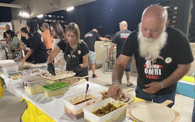Hostage father Dani Miran, far right, with a long beard grown while his son is held hostage, works with other volunteers at a pizza dinner he organized at the Hostages Forum in November 2024 (Jessica Steinberg/Times of Israel)