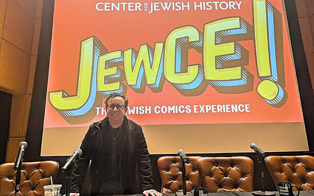 Kaplan poses under the JewCE logo at JewCE: The Jewish Comics Experience at the Center for Jewish History in Manhattan, November 10, 2024. (Jay Deitcher)