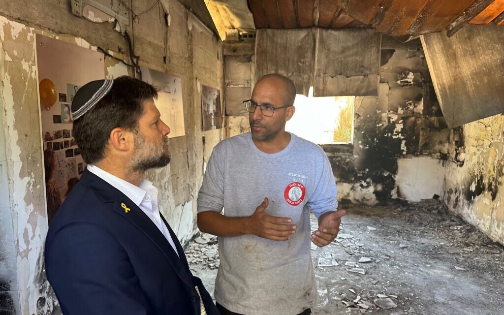Finance Minister Bezalel Smotrich, left, visits a home in Nir Oz destroyed in Hamas's October 7, 2023, onslaught, accompanied by Nir Metzger, son of slain hostage Yoram Metzger, in an image from the visit provided jointly by Smotrich's office and Nir Oz, November 12, 2024. (Courtesy)
