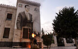 A Syrian anti-government fighter shoots against a large banner bearing a picture of Syria's President Bashar al-Assad, hanging on the facade of a municipal building in the west-central city of Hama on December 5, 2024. (Rami al SAYED / AFP)