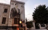 A Syrian anti-government fighter shoots at a large banner bearing a picture of Syria's deposed President Bashar Assad, hanging on the facade of a municipal building in the west-central city of Hama on December 5, 2024. (Bakr Alkasem/AFP)
