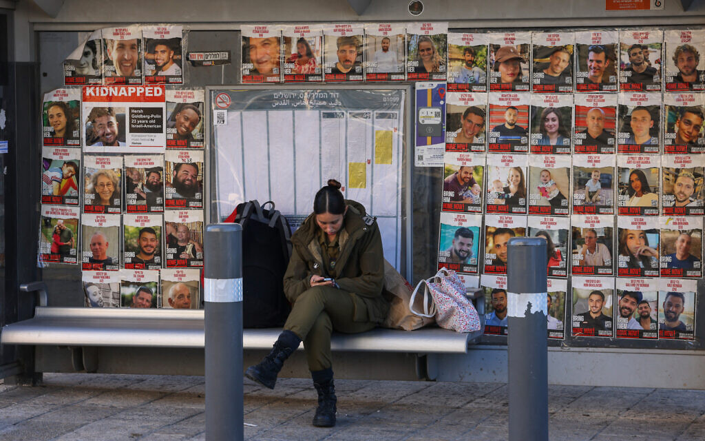 A member of the Israeli military checks her phone as she sits at a bus stop covered with portraits of Israelis held hostage in Gaza, on King George Street in Jerusalem on December 5, 2024. (Hazem BADER / AFP)
