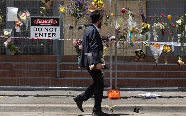 Illustrative: A member of the Jewish community reads messages attached to a fence where flowers have been left at the Adass Israel Synagogue in the Melbourne suburb of Ripponlea after an arson there, December 9, 2024. (Martin KEEP / AFP)