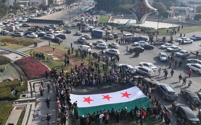 People celebrate holding a large Syrian opposition flag at Umayyad Square in Damascus on December 9, 2024. (OMAR HAJ KADOUR / AFP)