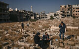 People pray by the grave of a relative in a damaged cemetery at the Yarmouk camp for Palestinian refugees in the south of Damascus on December 14, 2024. (Aris MESSINIS / AFP)