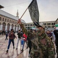Illustrative: A masked rebel fighter from the opposition group Hayat Tahrir al-Sham waves a jihadist flag in the courtyard of the Umayyad Mosque in the old walled city of Damascus, Syria, on December 10, 2024. (AP Photo/ Hussein Malla)