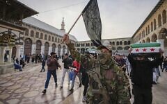 A masked opposition fighter carries a flag of Hayat Tahrir al-Sham in the courtyard of the Umayyad Mosque in the old walled city of Damascus, Syria, on December 10, 2024. (AP Photo/ Hussein Malla)