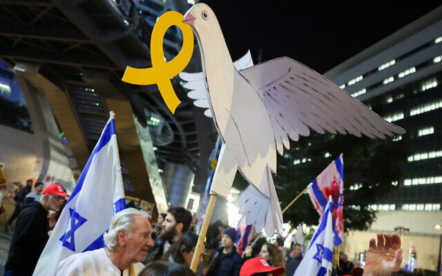 A protester holds a placard with a dove carrying a yellow ribbon, symbolizing solidarity with the hostages taken by Hama-led terrorists during the October 7, 2023 attack, during a demonstration calling for their release outside the Defense Ministry headquarters in Tel Aviv on January 4, 2025 (Jack GUEZ / AFP)
