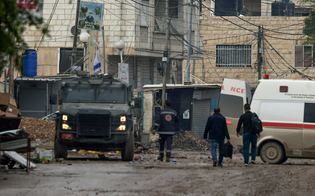 Men walk between an ambulance and an Israeli military vehicle in Jenin in the West Bank on January 24, 2025, during a large-scale Israeli army operation in the area. (Jaafar Ashtiyeh/AFP)