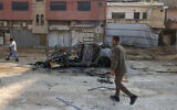 Palestinians walk near a car that was destroyed in an Israeli airstrike in the Nur Shams refugee camp near Tulkarem in West Bank on January 27, 2025. (Jaafar ASHTIYEH / AFP)
