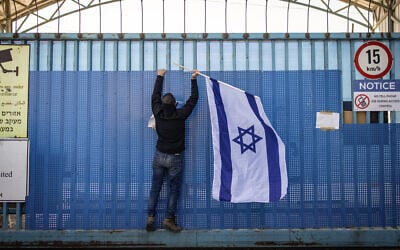 A right-wing activist hangs a national flag at the shuttered gate of the United Nations Relief and Works Agency UNRWA's West Bank Field Office in Jerusalem on January 30, 2025. (John Wessels/AFP)