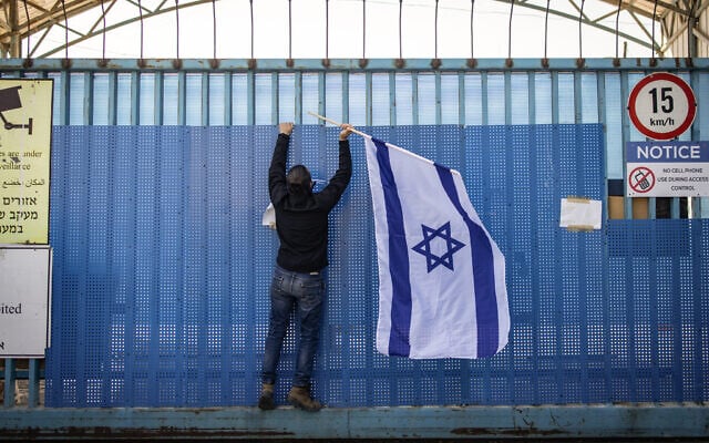 A right-wing activist hangs a national flag at the shuttered gate of the United Nations Relief and Works Agency UNRWA's West Bank Field Office in Jerusalem on January 30, 2025. (John Wessels/AFP)