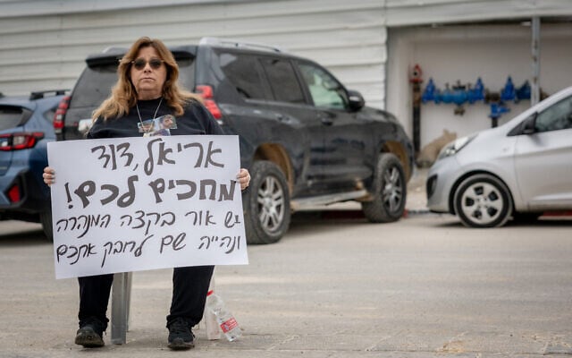 Sylvia Cunio, mother of David and Ariel Cunio who are held hostage by Hamas terrorists in Gaza, holds a sign as she sits outside the Prime Minister's Office in Jerusalem, January 22, 2025 (Chaim Goldberg/FLASH90)